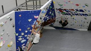 Image of students climbing on the NMT抱石墙. The wall is made up of alternating blue and white panels.